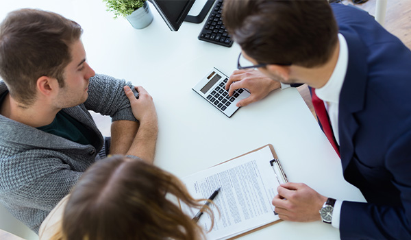 Three well-dressed professional individuals negotiating prices around a calculator and paperwork