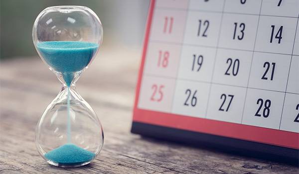 Hourglass with blue sand about a third of the way passed, with a month calendar in the back and some days highlighted in red.