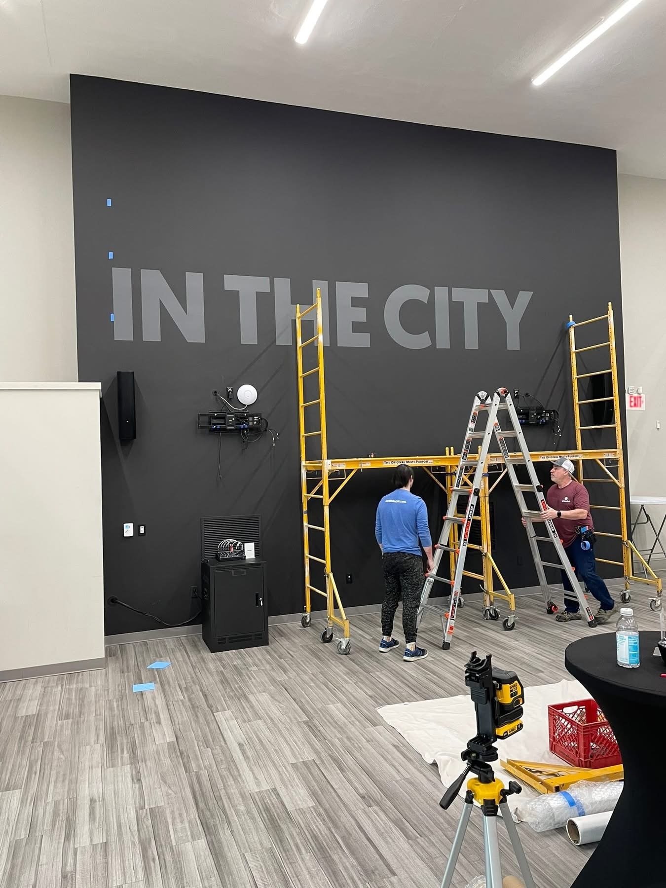 Two men working with ladders and scaffolding to install large, raised signage