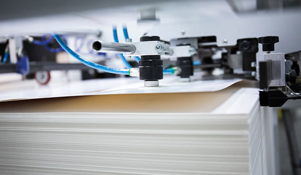 Up close shot of lamination finish being added to the top page of a stack of pages by complex machinery